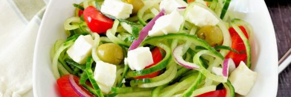 Greek Salad with cucumber noodles close up in white bowl on a rustic wood background